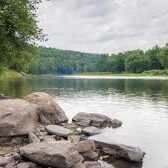 A body of water with trees and rocks in the foreground.